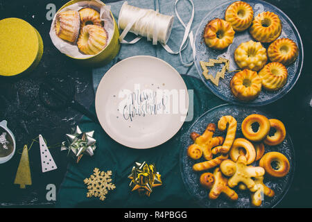 Weihnachten Platte mit gedruckten Grüße eingekreist von Mini bundt Cake und Dekoration auf einem Brett mit Weihnachten Dekoration, eine goldene Paket und Schere, t Stockfoto