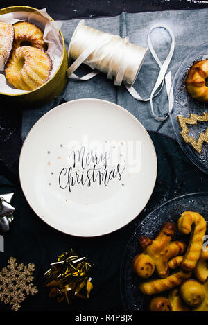 Weihnachten Platte mit gedruckten Grüße eingekreist von Mini bundt Cake und Dekoration auf einem Brett mit Weihnachten Dekoration, eine goldene Paket und Schere, t Stockfoto