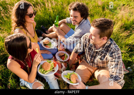 Freunde sitzen im Gras und in Burger am Grillfest Stockfoto