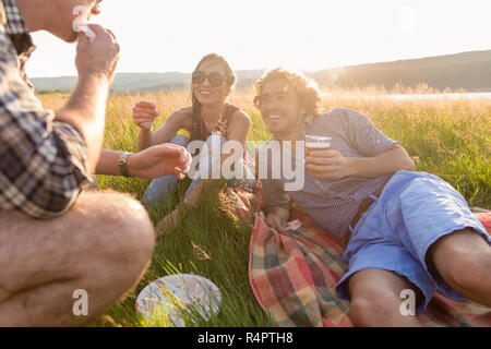 Freunde sitzen im Gras und in Burger am Grillfest Stockfoto