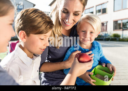 Mutter und Kinder in vegetarisches Mittagessen mit Streifen von Paprika in der Schule Stockfoto