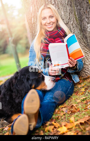 Frau mit Hund lesen Buch im Herbst Park Stockfoto