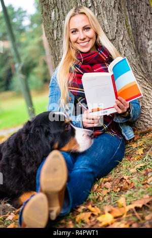 Frau mit Hund lesen Buch im Herbst Park Stockfoto