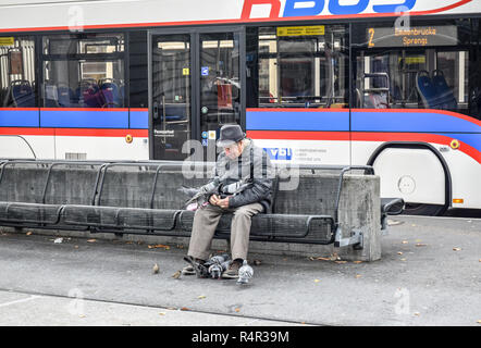 Ein einsamer Mann sitzt auf einer Bank am Bahnhofplatz in Luzern, Schweiz - - Fütterung der Vögel. Stockfoto