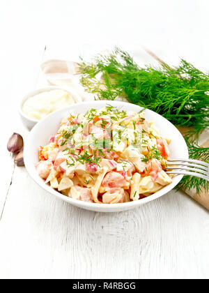 Salat von Crab Sticks, Käse, Knoblauch, Eier und Tomaten, gekleidet mit Mayonnaise in einer Platte, Handtuch und Petersilie auf einem Holzbrett Hintergrund Stockfoto