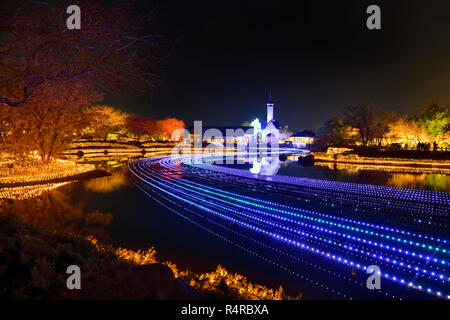 Nabana keine Sato Blumengarten, Winter Beleuchtung. Strom der Lichter über den Teich mit Licht bis Kapelle im Hintergrund. Stockfoto