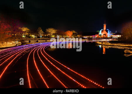 Nabana keine Sato Blumengarten, Winter Beleuchtung. Strom der Lichter über den Teich mit Licht bis Kapelle im Hintergrund. Stockfoto