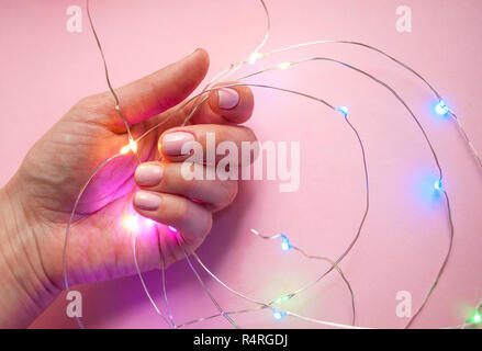Die junge Frau mit schönen Maniküre holding Lichterkette auf rosa Hintergrund. Stockfoto