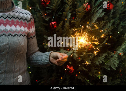 Frau in Form gestrickter Pullover Wunderkerzen halten vor dem Weihnachtsbaum Stockfoto