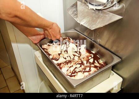 Frau an Ice Cream Factory arbeitet Dekorationen von cremiger Vanille Eis mit Schokolade Dressing in Stahl container. Gießen von Schokolade. Stockfoto