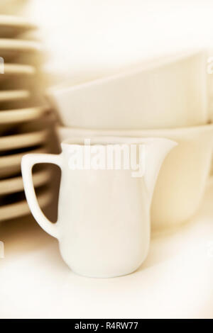 Kleine Kanne und weiße Tassen Kaffee mit Service Platte im Regal auf weißem Hintergrund. Kaffeetassen mit Tabletts in der Coffee Bar. Weißes Geschirr. Stockfoto