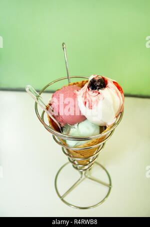 Eis Inhaber. Erdbeere, Minze, Vanille mit Sauerkirschen Eis in große Waffel Kegel in Halter, Löffel. Frisch gebackenes Eis Waffel Kegel. Stockfoto