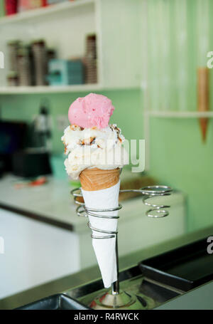 Eis Inhaber. Erdbeere, Vanille mit getrockneten Früchten und weiße Schokolade Eis in große Waffel Kegel in Halter mit Plastiklöffel. Eis. Stockfoto