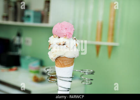 Eis Inhaber. Erdbeere, Vanille mit getrockneten Früchten und weiße Schokolade Eis in große Waffel Kegel in Halter mit Plastiklöffel. Eis. Stockfoto