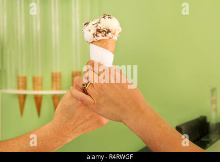 Zwei weibliche Hände halten Ein mit Schokolade Vanille Eis. Frau verkauft Eis in Konditorei und halten Eis in der Waffel Kegel. Stockfoto