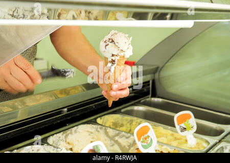 Weibliche Hand hält ein Vanille mit getrockneten Früchten, Eis in der Waffel Kegel. Eis Kühlschrank mit Stahl Service Container im Hintergrund. Stockfoto