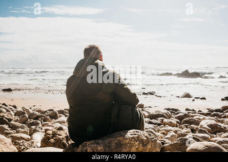 Ein Mann mit einem Rucksack oder ein Tourist oder ein Reisender in der Einsamkeit bewundert einen schönen Blick auf den Atlantik in Portugal. Suche nach Seele oder die Einheit mit der Natur. Stockfoto