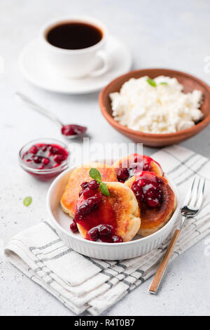 Quark Krapfen oder syrniki mit Preiselbeersoße auf weissem Teller mit schwarzem Kaffee. Selektiver Fokus Stockfoto