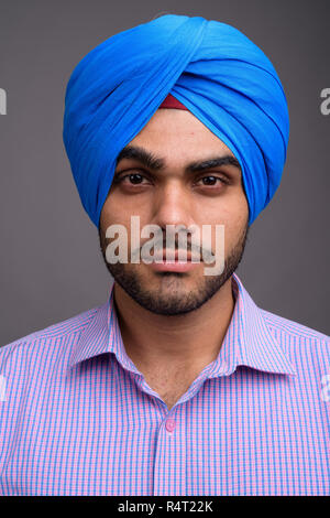 Junge hübscher indischer Geschäftsmann tragen Turban gegen Grau ba Stockfoto