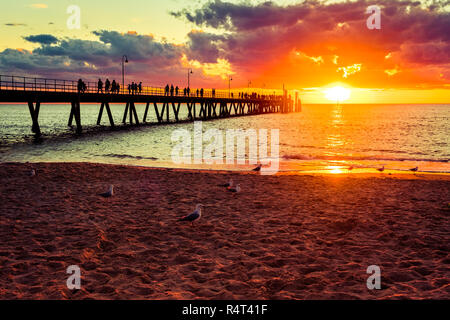 Strand von Glenelg mit Menschen zu Fuß entlang der Steg bei Sonnenuntergang, South Australia. Stockfoto