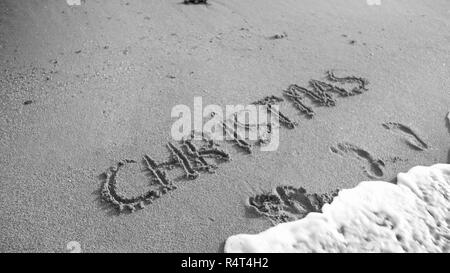 Schwarz-weiß Bild von Wort Weihnachten auf nassen San am Strand geschrieben. Sea Wave über fließende. Konzept der Winterferien, neues Jahr und Tourismus Stockfoto