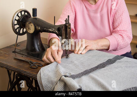 Ein altes weißes Haar Frau näht auf einer alten Nähmaschine. Stockfoto