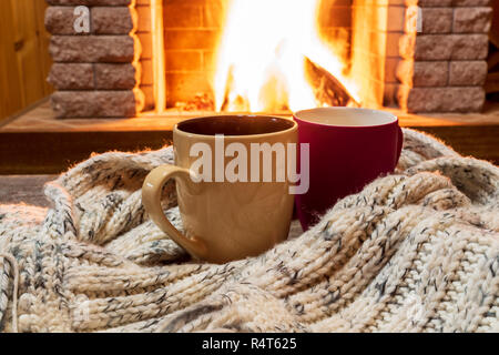 Zwei Becher mit heißem Tee und gemütlich warmen Schal in der Nähe von Kamin, im Landhaus, winter Urlaub, horizontal. Stockfoto