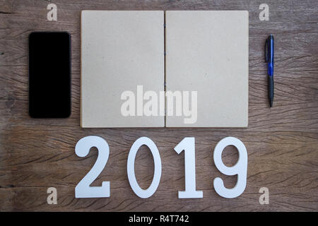 Ihre Arbeit Plan Konzept Fokus: Ansicht von Oben, flach Bürobedarf smartphone, Notizbuch und Stift mit einem Holz Nummer 2019 auf Holz Tisch. Persönliche Arbeit Stockfoto