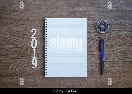 Ihre Arbeit Plan Konzept Fokus: Ansicht von Oben, flach Bürobedarf Notizbuch, Stift und Kompass mit einem Schnitt Holz Nummer 2019 auf Holz Tisch legen. Persönliche Arbeit Sp Stockfoto