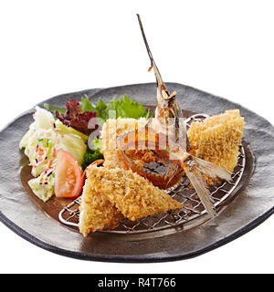 Frittiertem Fisch auf schwarzem Teller mit Tomaten und Salat Stockfoto
