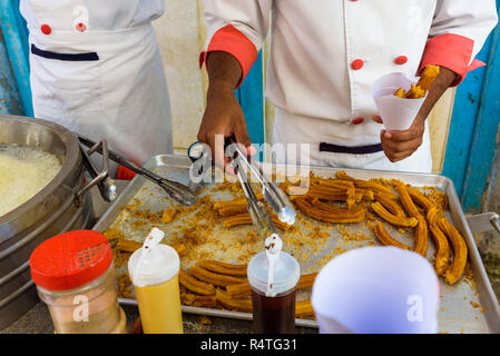 Kubanischen Männer mit einem Straße Warenkorb Verkauf und Vorbereitung Churros in Havanna. Churros Vorbereitung mit Schokolade. Frittieren Churros. Stockfoto