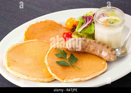 Gebratene Würstchen mit Salat, Brot und Obst auf weißem Teller Stockfoto