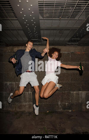 Portrait exuberant junges Paar Bier trinken und Springen Stockfoto