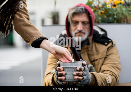 Nicht erkennbare Frau Geld geben für obdachlose Bettler sitzen draußen in der Stadt. Stockfoto