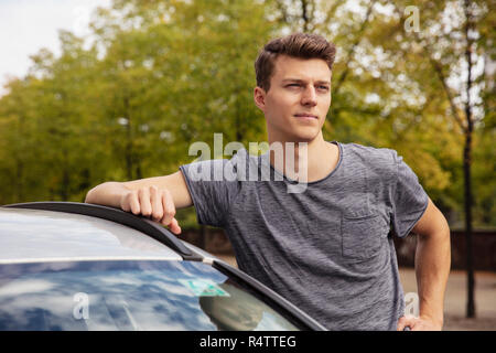 Porträt junger Mann lehnte sich auf dem Auto, Sie suchen Stockfoto