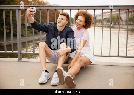 Junges Paar unter selfie mit Fotohandy auf städtischen Brücke Stockfoto