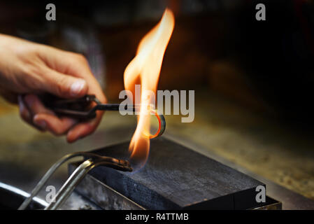 Goldschmied Hände glühen einen goldenen Ring in einer Gasflamme, mit Kopie Raum schließen in den dunklen Hintergrund, ausgewählte konzentrieren, enge Tiefenschärfe Stockfoto