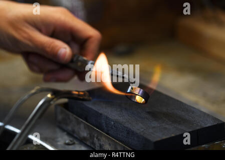 Hand eines Goldschmieds hält einen goldenen Ring mit Pinzette in einer Gasflamme zu Leuchten es, Platz kopieren in den dunklen Hintergrund, ausgewählte konzentrieren, schmale tiefe der fi Stockfoto