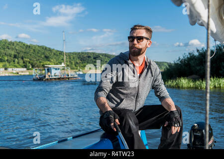 Ein Mann mit Sonnenbrille und legere Kleidung, als er ein kleines Beiboot rund um einen See oder Fluss Laufwerke Stockfoto