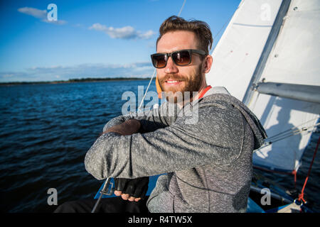 Stattlicher Mann mit der Yacht zu reisen. Casual Outfit, Mann in Grau hoodie gekleidet, Frühling, bärtigen Mann mit Sonnenbrille auf dem Boot. Stockfoto