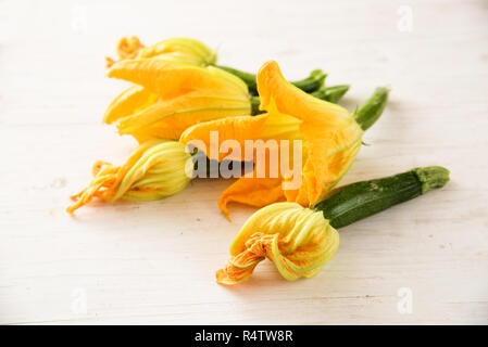 Zucchini und Zucchiniblüten auf weißem Holz- Tabelle für eine mediterrane Vorspeise, ausgewählte konzentrieren, sehr enge Tiefenschärfe Stockfoto