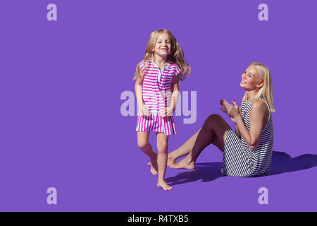 Portrait verspielt Mutter und Tochter in gestreiften Kleider gegen lila Hintergrund Stockfoto