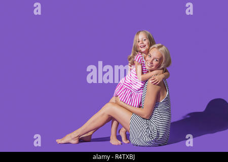 Portrait lächelnde Mutter und Tochter in gestreiften Kleider umarmen gegen lila Hintergrund Stockfoto