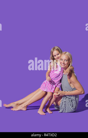 Portrait lächelnde Mutter und Tochter umarmen in gestreiften Kleider gegen lila Hintergrund Stockfoto