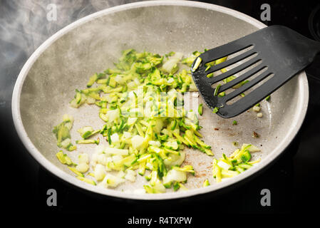 Geriebenen Zucchini und Zwiebeln in einer Pfanne mit Spachtel und Dampf auf einem schwarzen Herd gebraten, ausgewählte konzentrieren, enge Tiefenschärfe Stockfoto