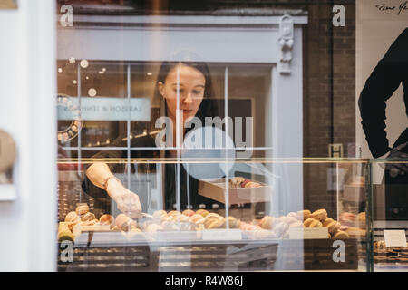 London, UK, November 21, 2018: Blick durch das Fenster einer Frau, Makronen in einem Kasten in eine handwerkliche Bäckerei in Covent Garden, einem Gebiet von Lo Stockfoto