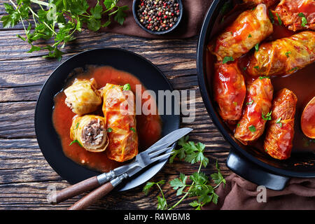 Kohlrouladen gefüllt mit Hackfleisch und Reis, zur Perfektion mit einer würzigen Tomatensauce in einem holländischen Ofen zubereitet und auf einem Teller mit Besteck serviert, vi Stockfoto