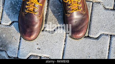 First Person Ansicht Schuhe. Winterspaziergang Konzept. Blick von oben auf braune Stiefel auf Kopfsteinpflaster Hintergrund Stockfoto