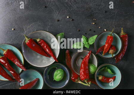 Viel chili peppers mit Basilikum und Pfefferkörner in Schalen auf eine rustikale Oberfläche, Stockfoto