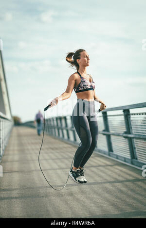 Junge Läuferin über Springseil und Übung auf einer Brücke über den Fluss springen, Vorbereitung für Morgen Workout. Stockfoto
